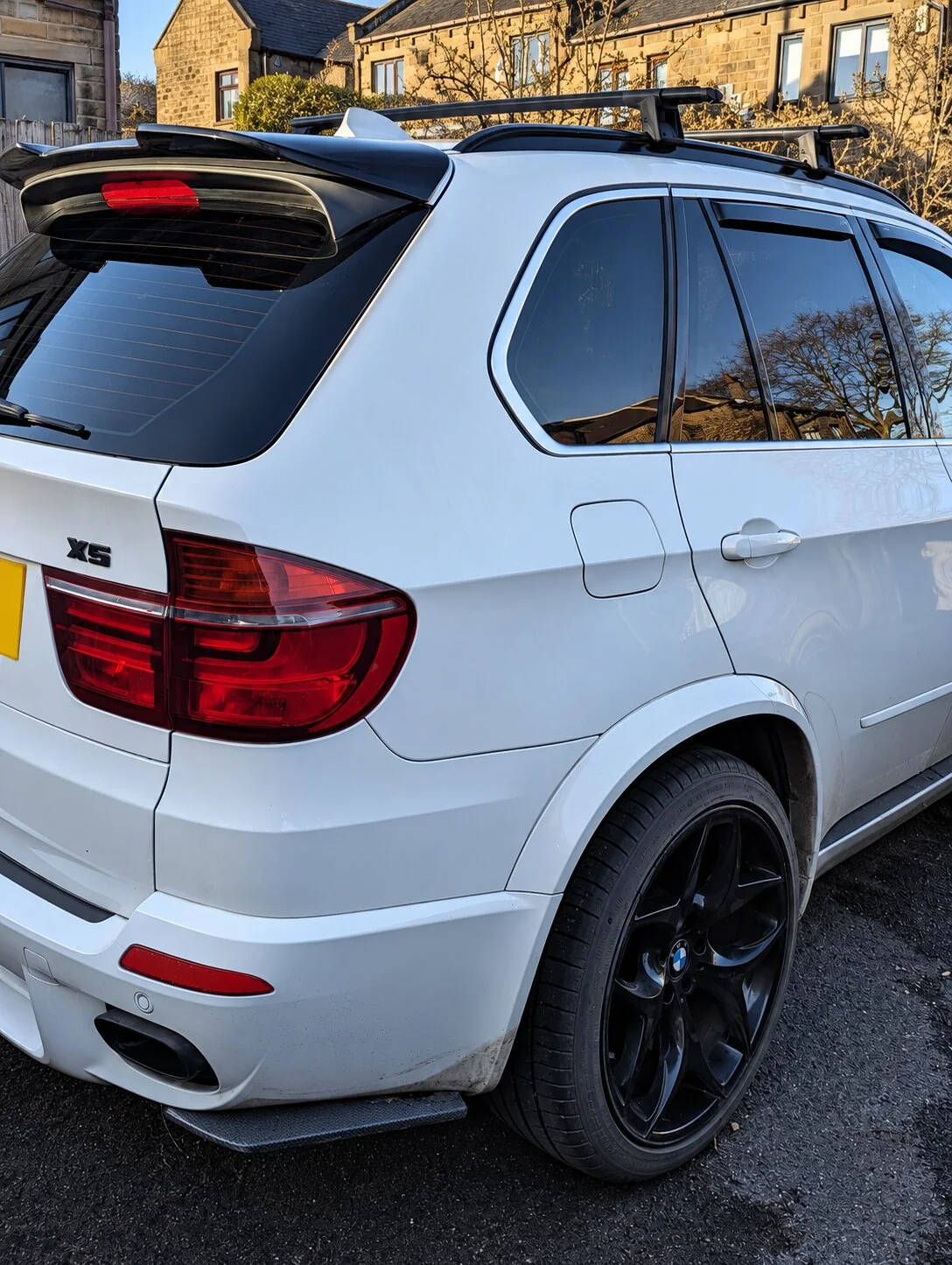 Rear three-quarter view of a white BMW X5 with a black rear roof spoiler
